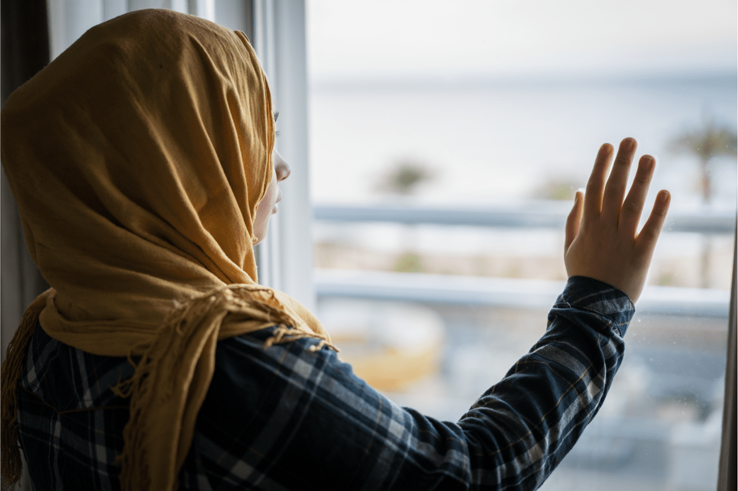 A arabic woman touching the window while watching outside